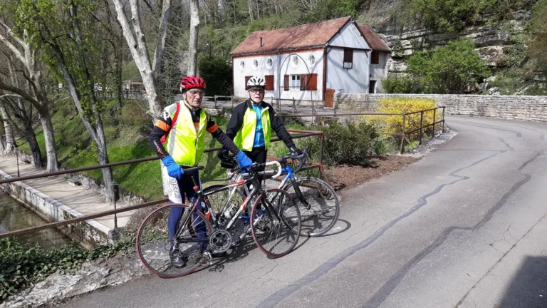 Deux cyclos en gilet jaune sur un pont, près d'une maison au bord de l'eau