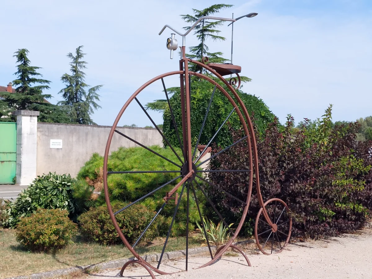 Sculpture d'un grand-bi en métal dans un massif fleuri