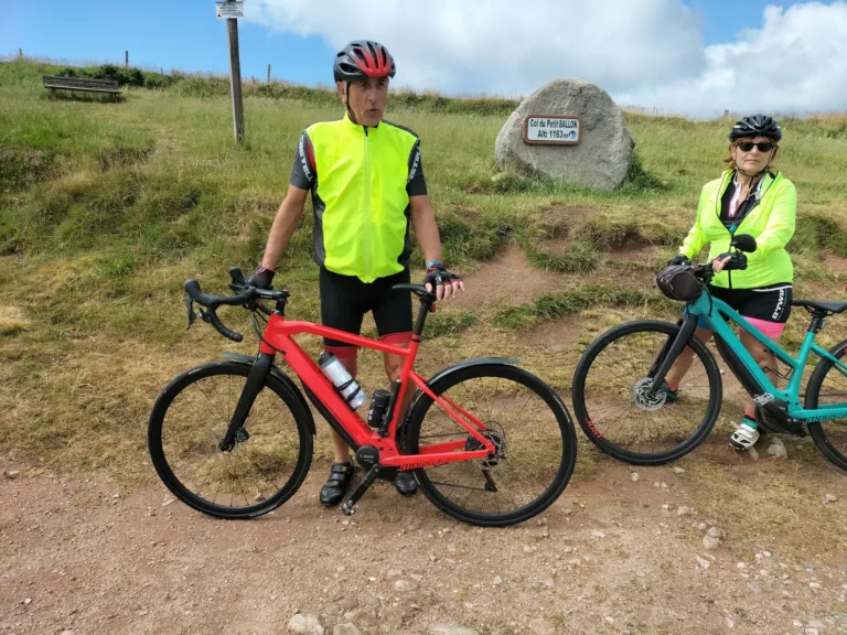 Deux cyclos et leurs vélos près d'une borne au sommet d'un col, en Alsace